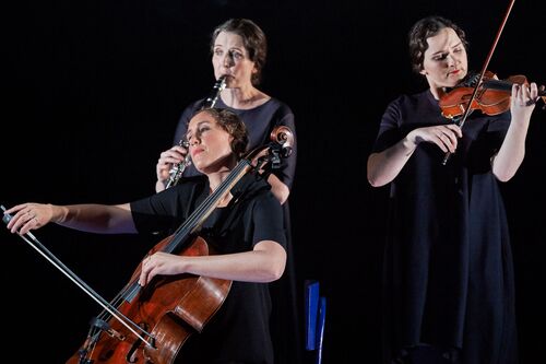 Three musicians playing instruments dressed in black on stage