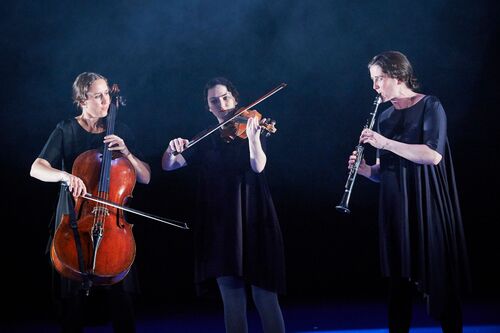 Three musicians playing instruments dressed in black on stage