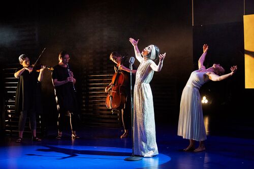 A figure singing into a microphone with another figure in movement mirroring behind