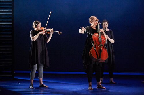 Three musicians playing instruments dressed in black on stage