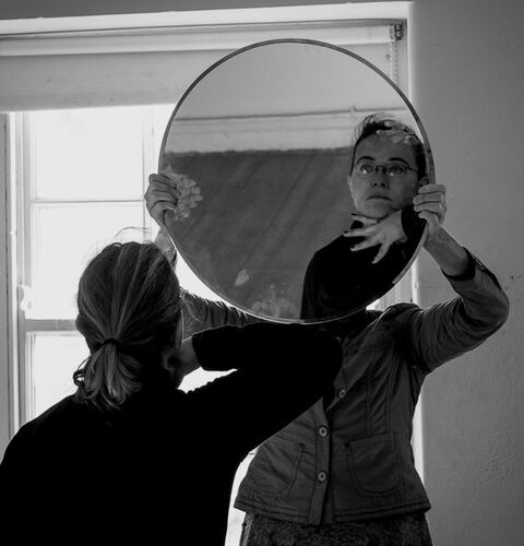 A figure reflected in a mirror being held by another participant