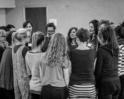An ensemble of women standing in a circle in black and white