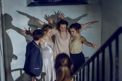 Four women with arms outstretched and overlapping with each other at the foot of a staircase