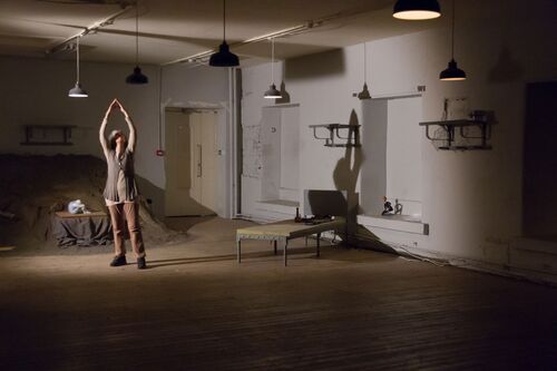 A single figure standing in an empty space with their shadow cast to the right of the image