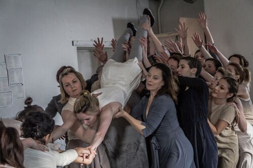 An ensemble of women lifting and reach towards one figure held above them