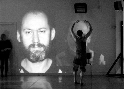 A figure in movement with a face projected on the wall beyond