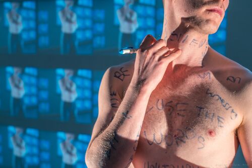 Ryan O'Neill's torso as he writes words on his skin with a marker