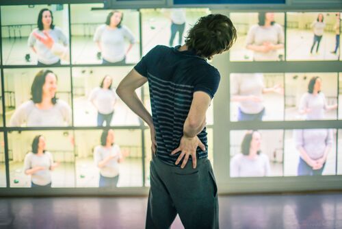 A figure in movement facing still shots in a grid projected on the wall
