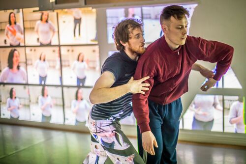 Two dancers in movement with projections along the wall behind them