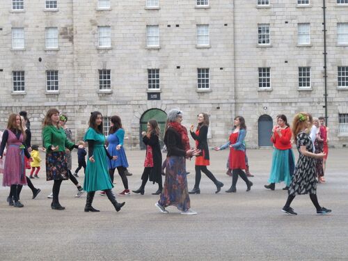 A group of women in different coloured dresses moving around the courtyard of Collin's Barracks