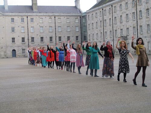 A line of women in different coloured dresses moving in single file