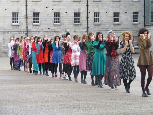 A line of women in different coloured dresses moving in single file