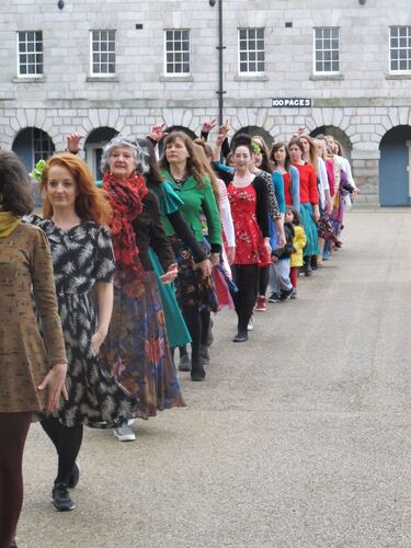 A line of women in different coloured dresses moving in single file