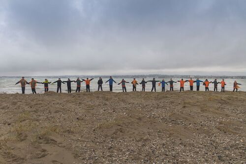 A chain of children with their arms outstretched along the coast seen from afar