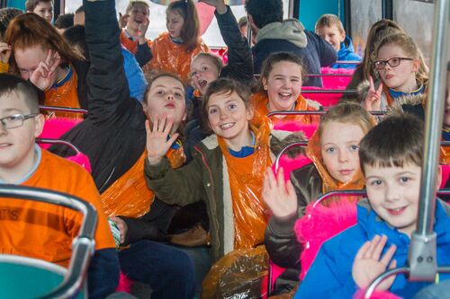 A group of children sitting on the upper deck of a bus waving to camera