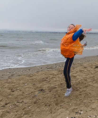 A child mid-leap on the beach wearing an orange rain poncho