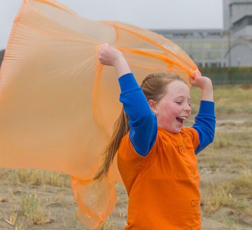 A child in an orange tshirt holding a plastic orange poncho in the wind overhead