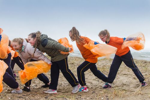 A group of children in movement on the beach with orange rain ponchos in their hands