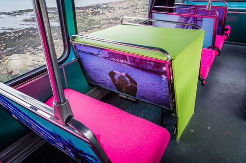 A view of the upper deck of a bus with screens fixed to the back of coloured seats