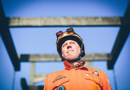 A figure dressed in orange with a blue sky behind