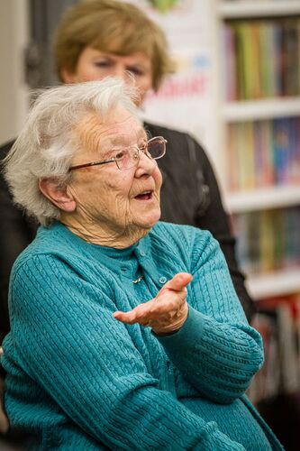 An older person seated, mid-speech