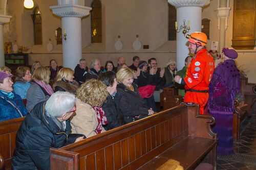 Two figures in bright colours in front of an audience seated in a church