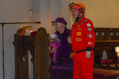 Two figures in purple and orange respectively standing with arms linked