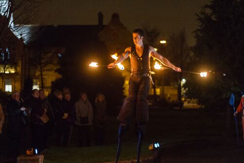 A figure outdoors on stilts with flaming batons in hand