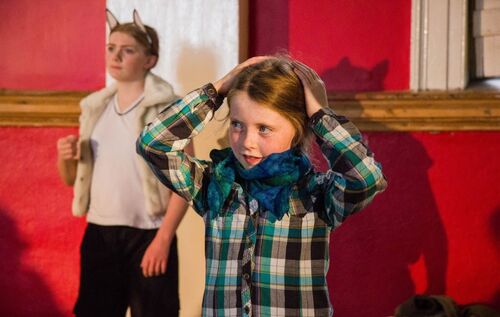 A young girl with her hands on her head and another child in the background wearing wolf ears