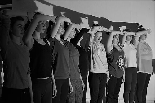 Participants standing in line each with one arm raised and bent at the elbow in black and white