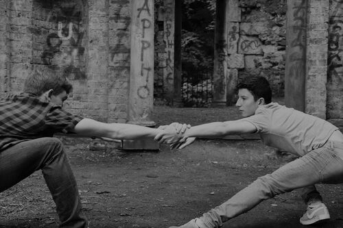 Two figures in movement with each other's hands clasped in the centre of the image