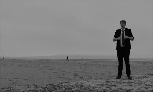A figure in a suit standing on an open stretch of beach