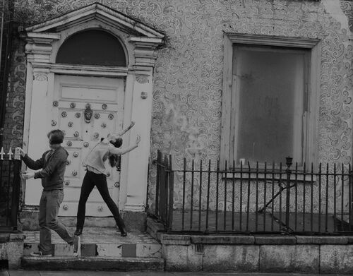 Two figures in movement outside an ornate doorway
