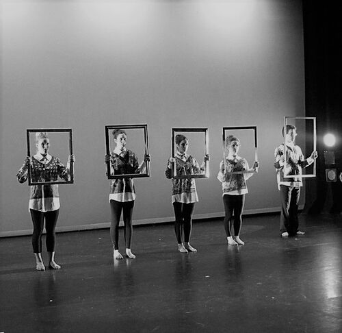An ensemble in a line on stage holding empty picture frames