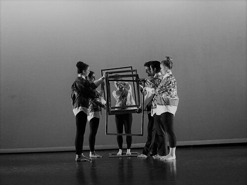 An ensemble in movement on stage with empty picture frames
