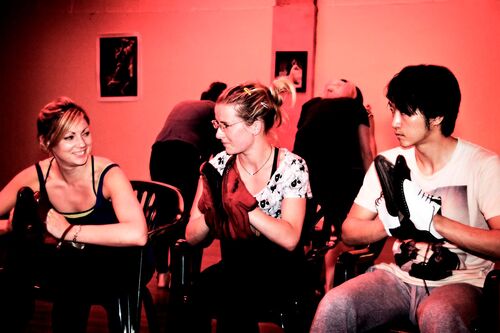 Three figures seated on chairs with shoes on their hands