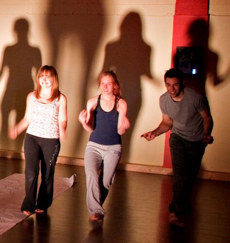 Three figures in movement with shadows cast on a wall behind them