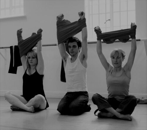 Three figures sitting cross legged in movement with jumpers raised above their heads
