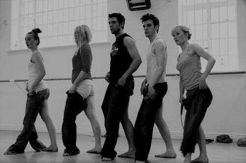 Five participants in a line in movement each with one leg through a pair of jeans