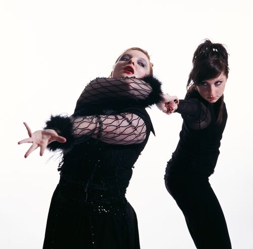Two figures in all black on a white backdrop in movement