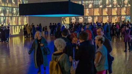 A gallery space full of audience members with projections along all walls
