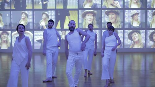 An ensemble in formation moving in space with projects on the walls behind them