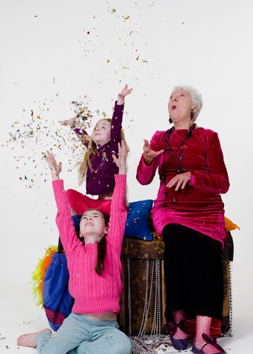 An older figure sitting on a chest having thrown confetti two children are reaching for