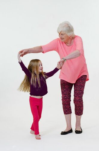 An older figure holding a child's hands above her head as she dances