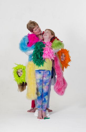 An older figure standing with three children wearing bright feather boas