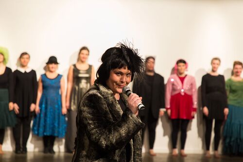 A participant with a microphone to their mouth with other participants lined up at the wall behind