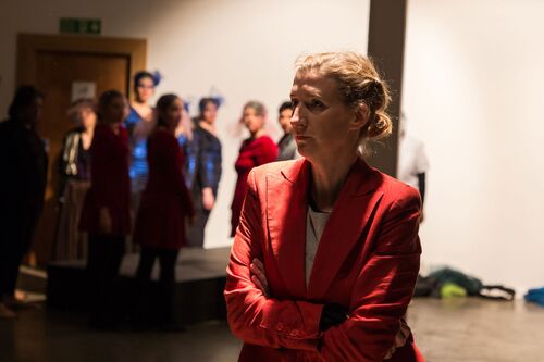 A participant with arms wrapped around herself and others observing her in the background