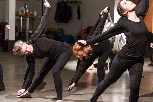 Three participants in movement reaching to the floor and up towards the ceiling