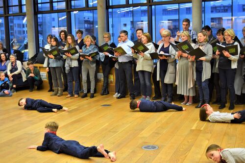 Young participants in movement on the floor while older participants stand singing from folders