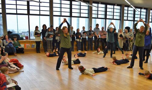 Young and older participants in movement with the children stretched on the floor